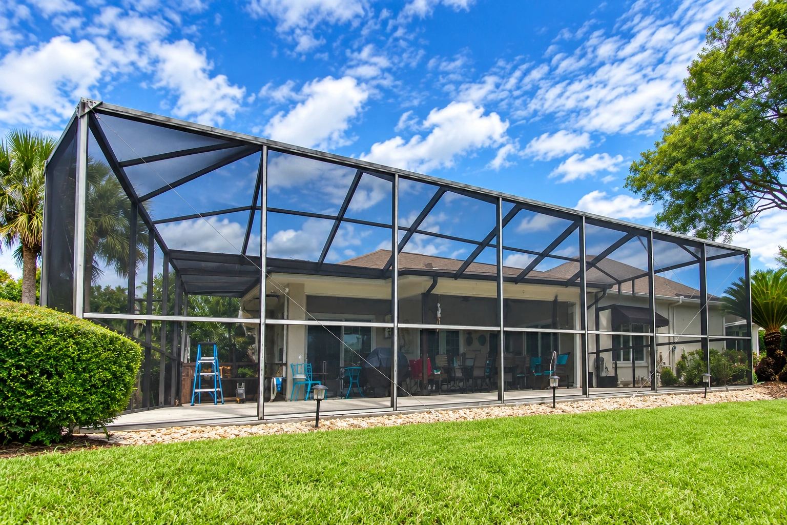 Large screened patio enclosure with a dark metal frame beside a house and lawn.