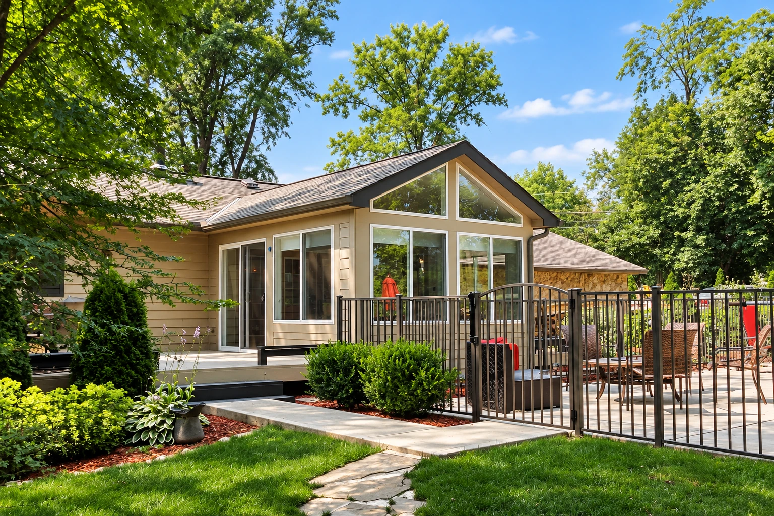 Sunroom addition with a peaked glass-fronted gable beside a fenced outdoor dining patio.