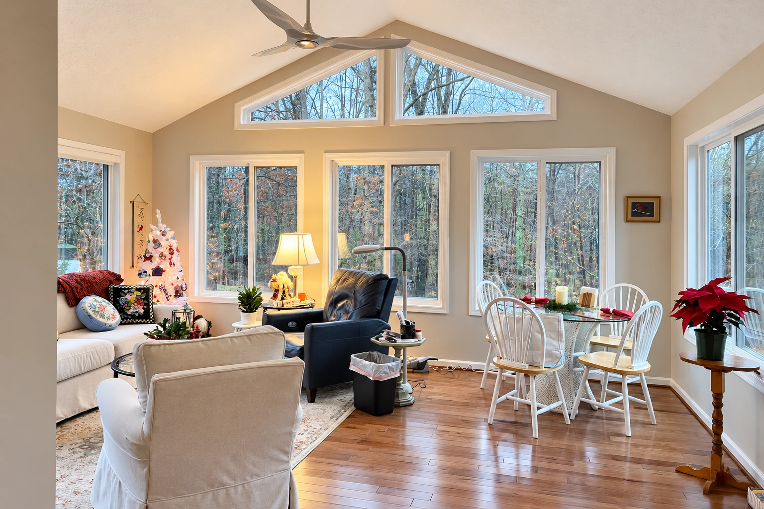 Remodeled sunroom with high triangular windows, a sitting area, and a dining table beside views of woodland.